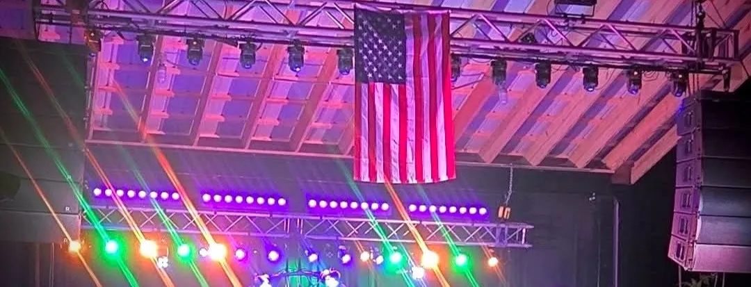 The Renegades performing on stage under purple and blue lights with the American flag and laser lights behind them