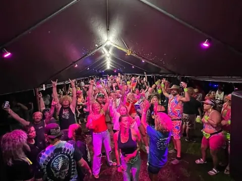 A crowd dancing under neon pink and purple lights inside the themed tent party
