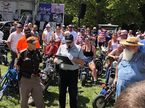 An official reads from a program to a crowd gathered with their mini bikes for opening ceremonies