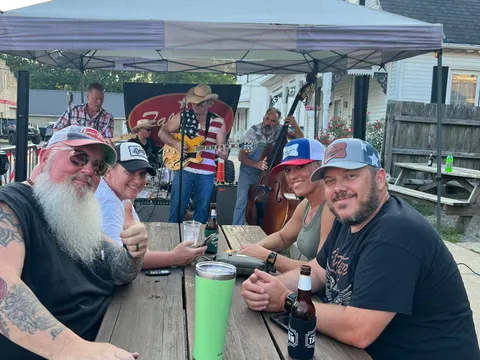 A band playing at Friendship Tavern's street party under a tent, with festival-goers seated at picnic tables